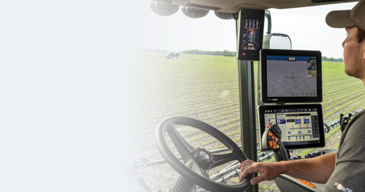 A person operates a tractor with multiple digital screens showing farming data in a field.