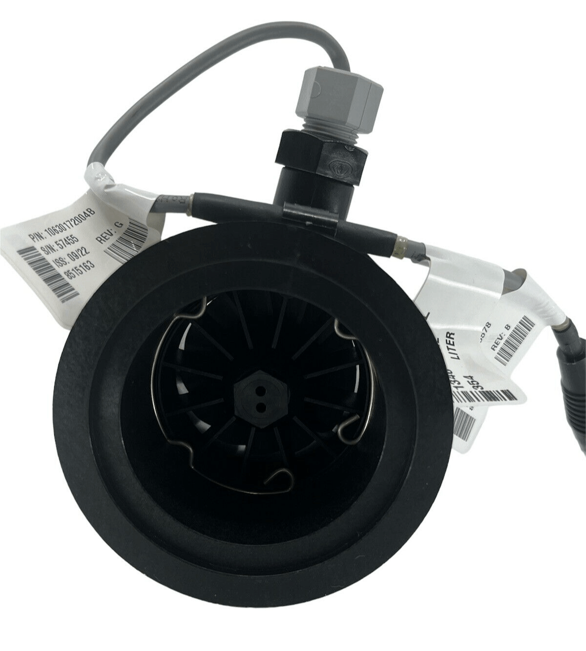 A black industrial component, the Raven RFM 100 Poly Flow Meter, featuring a circular opening and attached wires, is labeled with several tags. Designed for precision in agricultural applications, this unit integrates a robust polypropylene flow meter and has an M220 flange inlet and outlet to accommodate flows between 5 and 100 GPM.