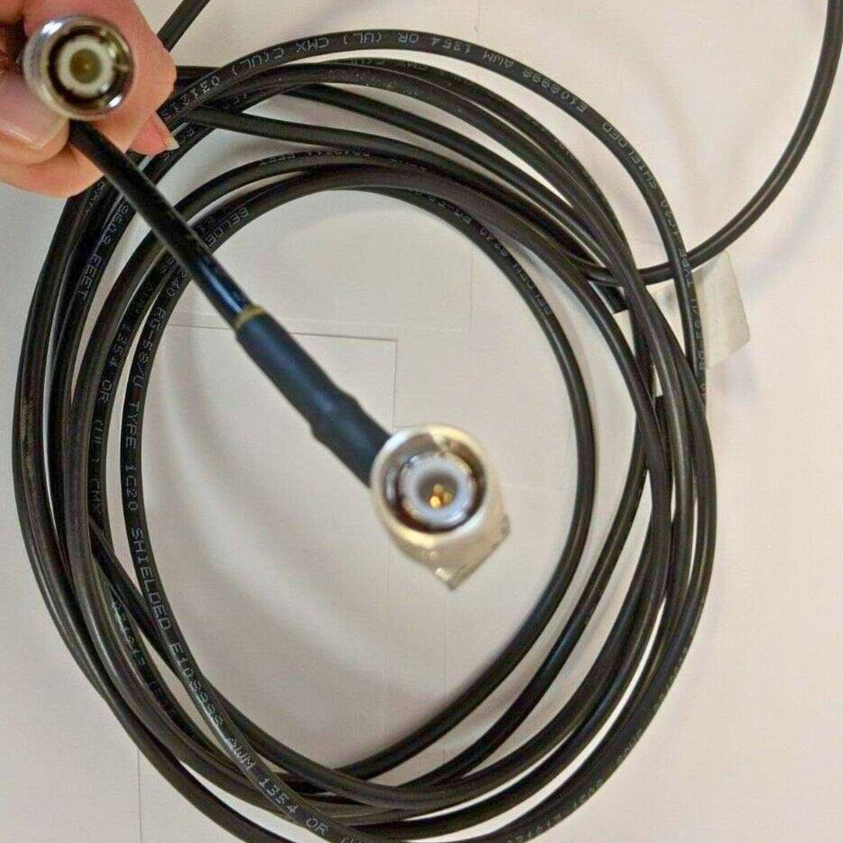 A hand holds a Raven Antenna Cable - 15' TNC Male to TNC Male, coiled on a white surface.