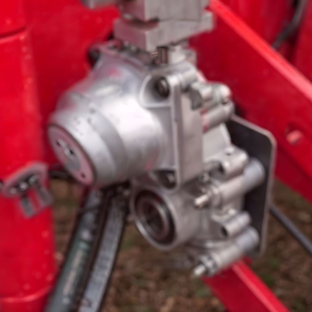 A close-up of a metal mechanical component attached to red machinery, featuring several bolts and hydraulic lines, likely part of the Raven OmniRow Hydraulic Motor 7/8In Hex 1 GPM IRC (416-8000-001), commonly used in precision agricultural applications.
