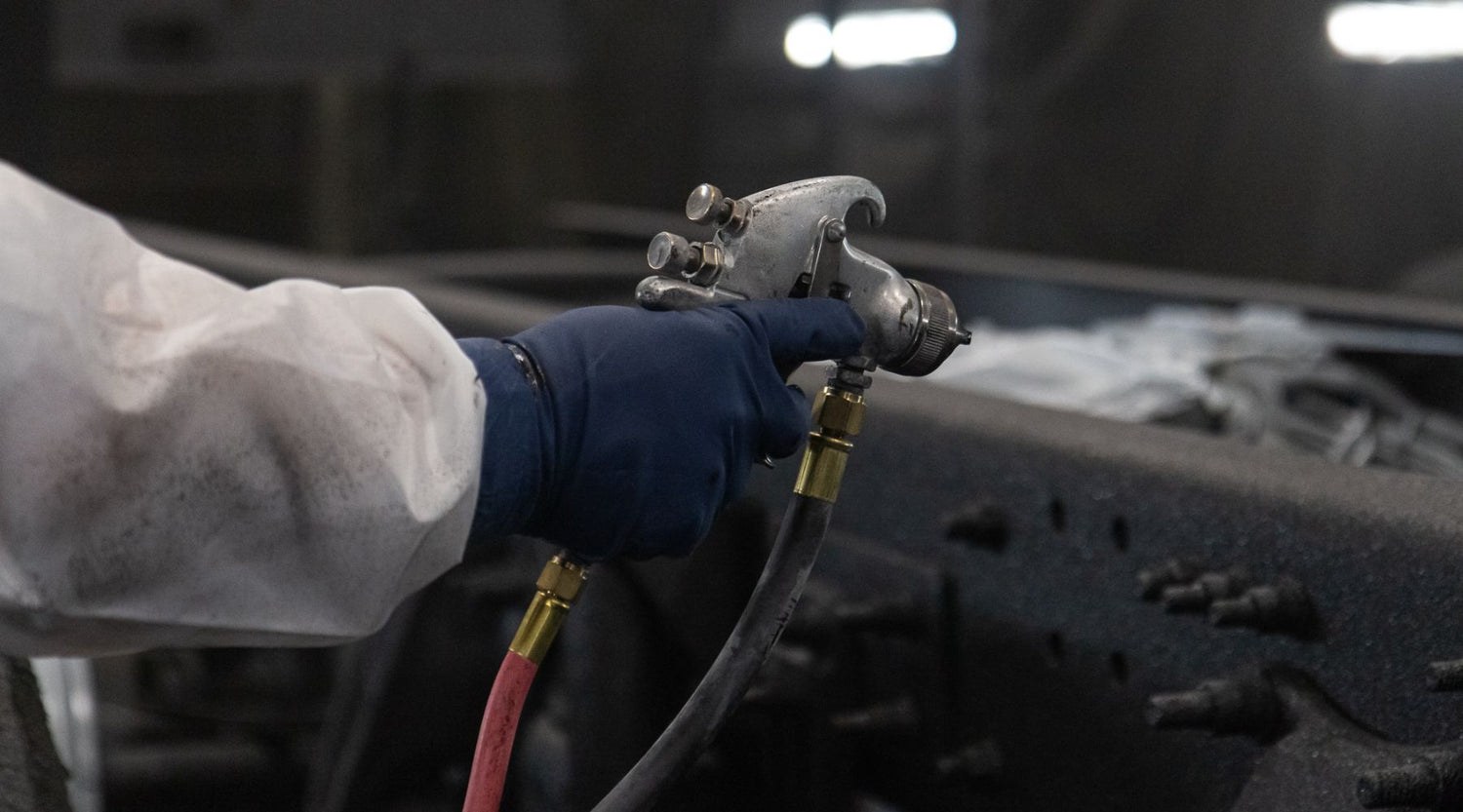 Person in protective clothing and gloves using a spray paint gun.