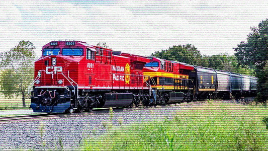 A red and black freight train labeled "Canadian Pacific" travels on tracks through a grassy area with trees in the background.