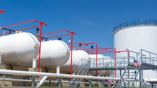 White cylindrical tanks with red pipes and stairs under a clear blue sky at an industrial site.