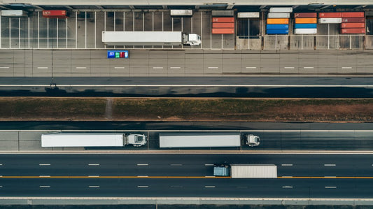 Aerial view of trucks parked and moving on the highway, with colorful containers lined up nearby.