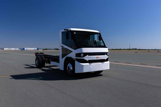 A white Motiv electric truck driving on a wide, empty road under a clear blue sky.