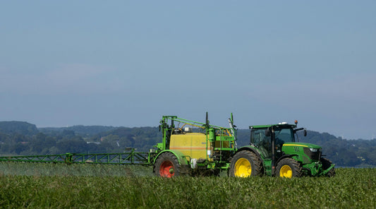 Green tractor with a large agricultural sprayer applying pesticides in a crop field under a clear sky